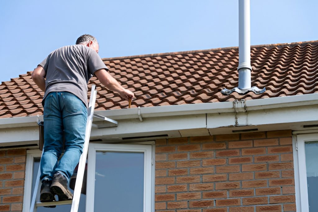 man standing on a ladder, cleaning gutters